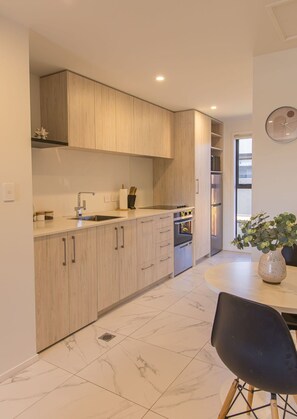 A modern kitchen with light wood cabinets, stainless steel appliances, and a marble floor. - Bright Studio Apartment on Macky Street (Lower Hutt)