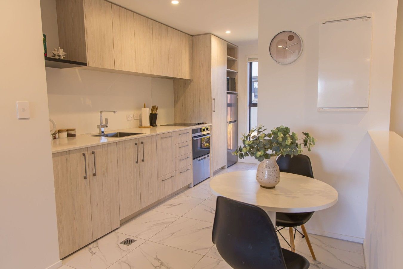 A modern kitchen with wooden cabinets, a dining table with chairs, and a potted plant.