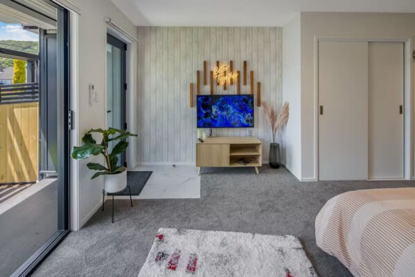 Une chambre moderne dotée d’un grand téléviseur, d’un meuble de rangement en bois et d’une porte-fenêtre coulissante donnant sur un balcon.