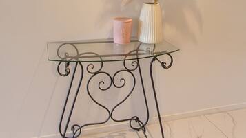 A glass console table with a mirror above it, a vase with dried pampas grass, and a pink candle.
