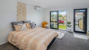 A bedroom with a large bed, a sliding glass door to a balcony, and a small table with a chair. - Macky Street Studio Retreat (Lower Hutt)