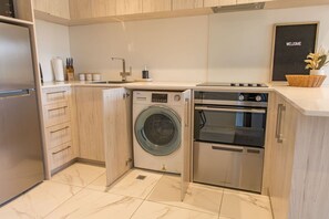 A compact kitchen with a washing machine, oven, and a 'WELCOME' sign. - Macky Street Studio Retreat (Lower Hutt)