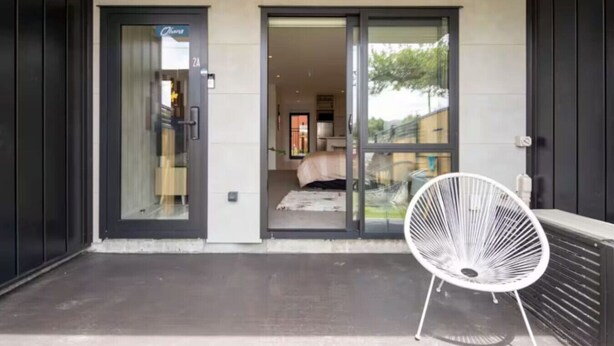 A modern building entrance with a glass door leading to a bedroom. - Macky Street Studio Retreat (Lower Hutt)
