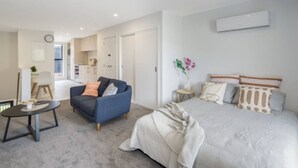 Ein modernes Schlafzimmer mit einem großen Bett, einer Couch, einem kleinen Tisch und einer Küchenzeile im Hintergrund.