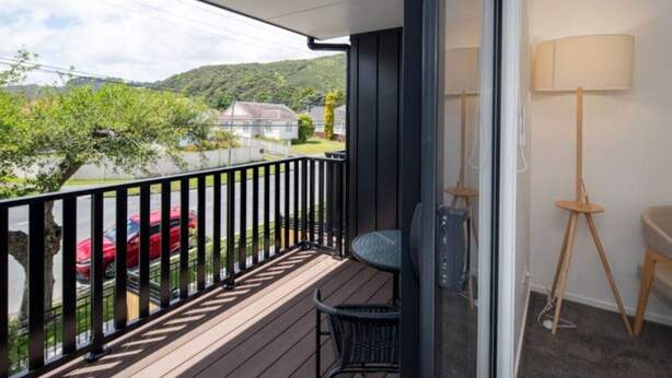Ein Balkon mit Blick auf ein rotes Auto und Grünflächen, ein Stuhl und eine Lampe.