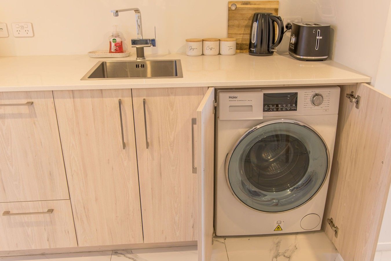 A compact kitchen with a built-in washing machine, a sink, and a coffee maker.