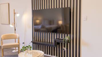 A modern living room with a flat-screen TV mounted on a black and white striped wall, a round coffee table with a plant, and a beige armchair.