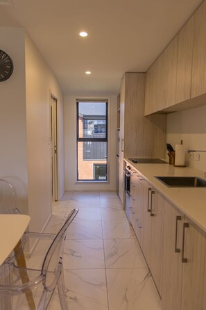 A modern kitchen with a window, a sink, and a dining area with a chair. - Peaceful Hideaway: Studio in Macky (Lower Hutt)