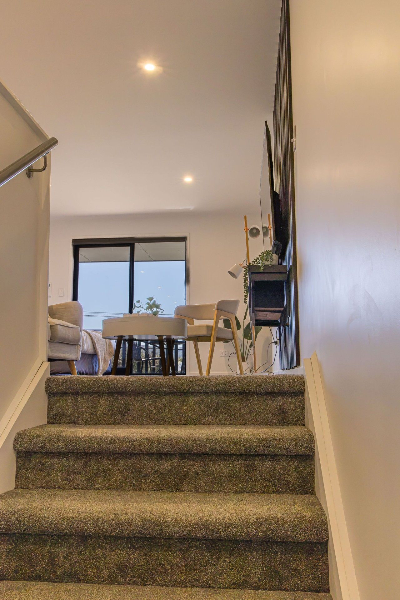 A staircase with carpeted steps leading to a dining area with a table and chairs.
