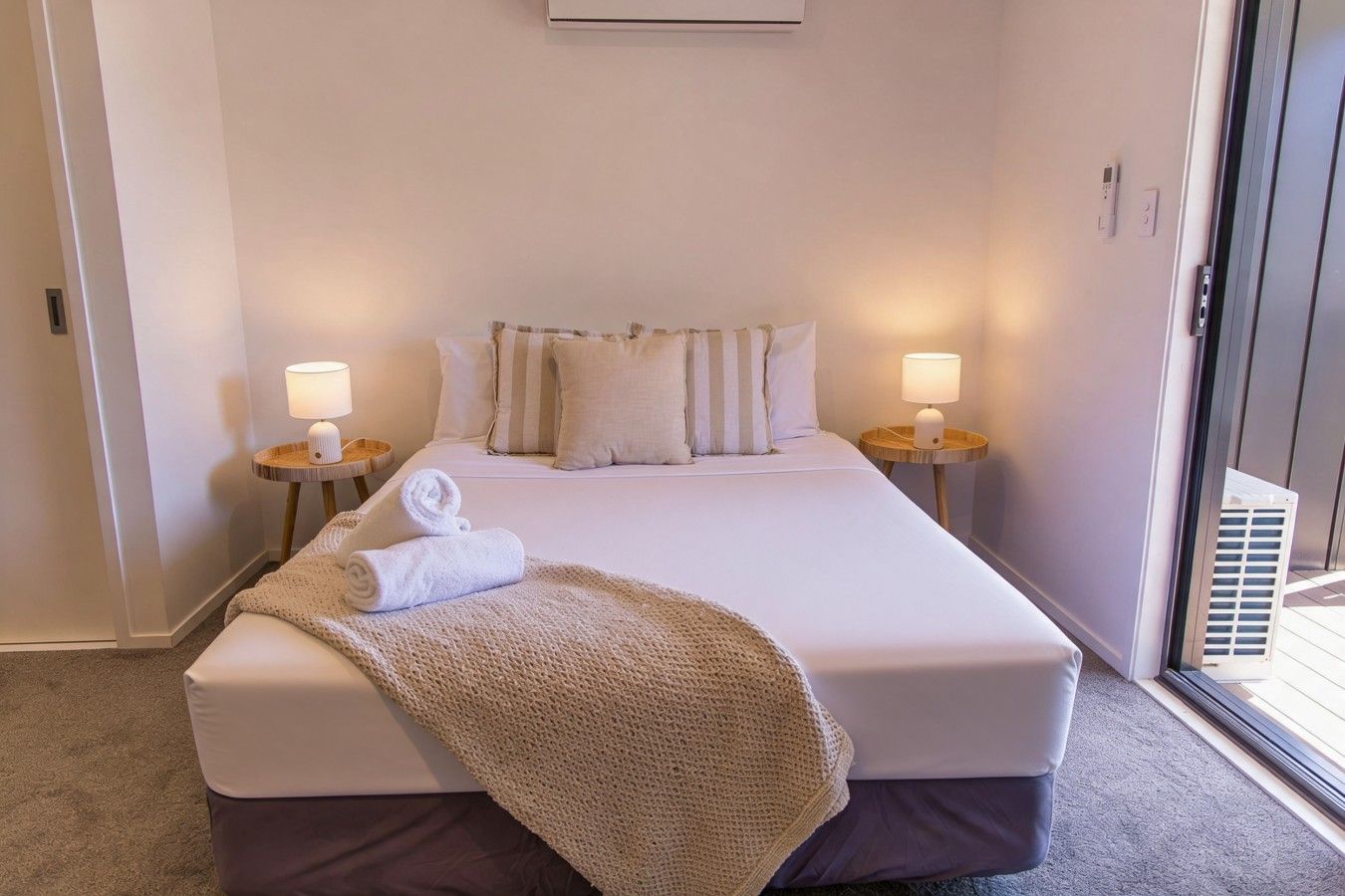 A hotel room with a bed, two bedside lamps, a window, and a door.