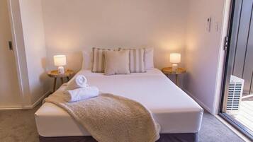 A hotel room with a bed, two bedside lamps, a window, and a door.