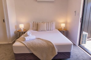 A hotel room with a bed, two bedside lamps, a window, and a door. - Peaceful Hideaway: Studio in Macky (Lower Hutt)