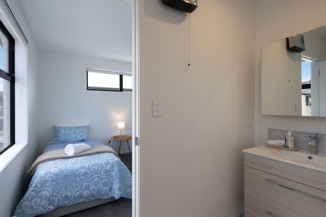 Un dormitorio con cama, mesita de noche, lámpara y un espejo grande sobre el tocador.