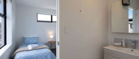 Un dormitorio con cama, mesita de noche, lámpara y un espejo grande sobre el tocador.