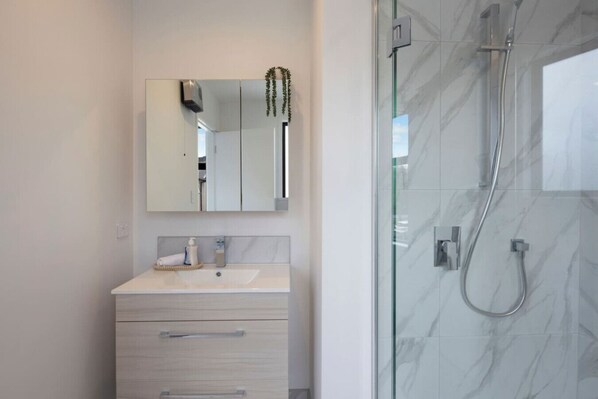 Une salle de bain moderne dotée d’une douche à parois de verre, d’un mur recouvert de carreaux de marbre et d’un meuble-lavabo minimaliste agrémenté d’un miroir et d’une serviette.