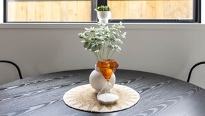 A round table with a woven placemat, a white vase with a geometric design, and a small potted plant. - Homely Haven in Trentham - 2BR (Upper Hutt)
