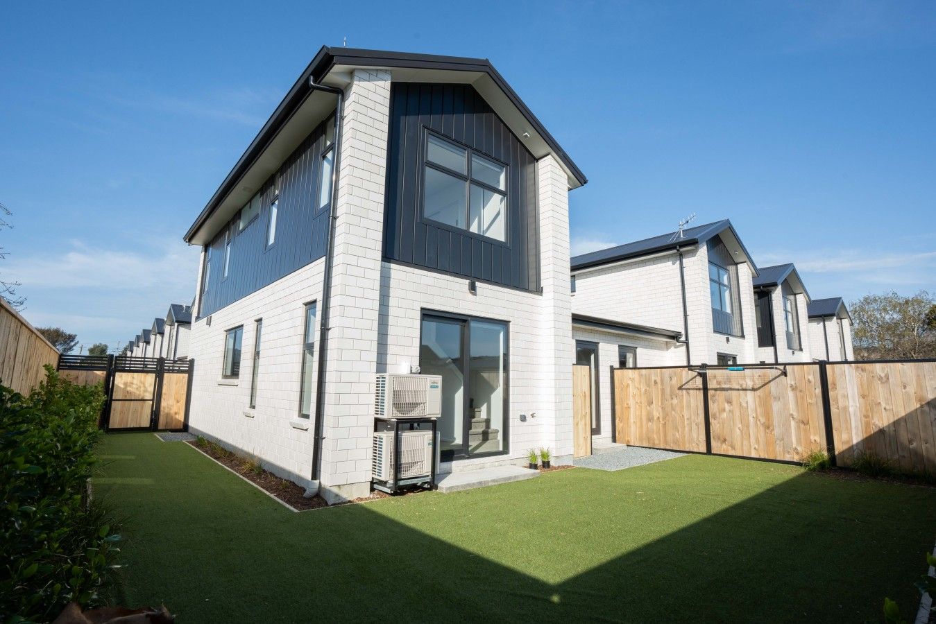 A modern two-story house with a flat roof, large windows, and a fenced backyard.