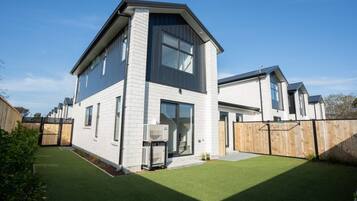 A modern two-story house with a flat roof, large windows, and a fenced backyard.