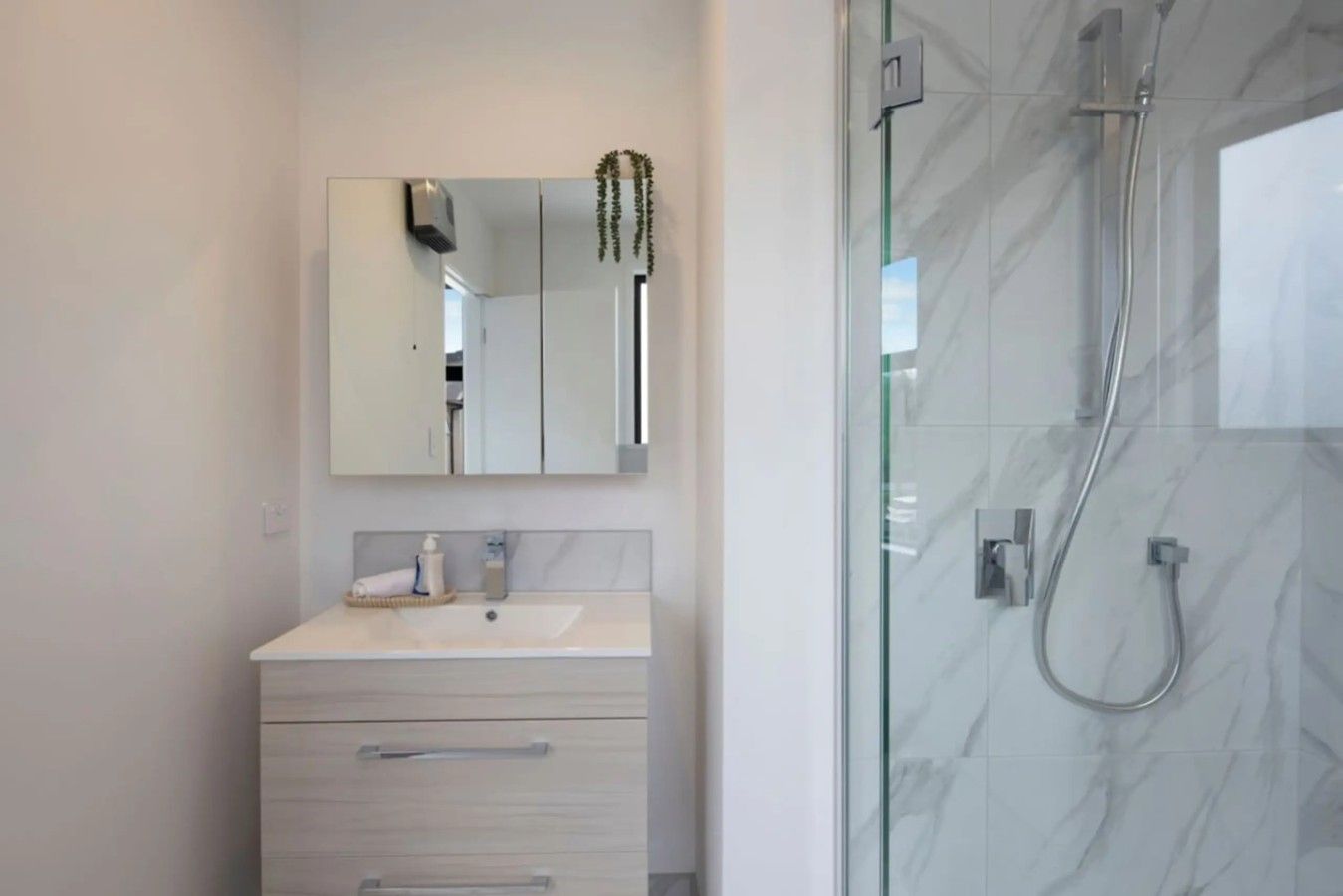Un baño moderno con cabina de ducha de vidrio, tocador con espejo y perchero.