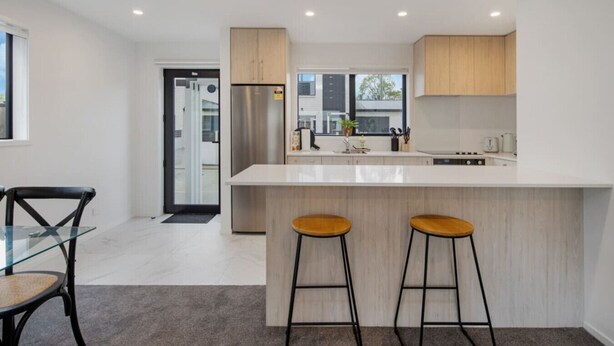 Une cuisine moderne dotée d’un grand îlot central, de deux tabourets et d’un coin repas avec une table et des chaises en verre.