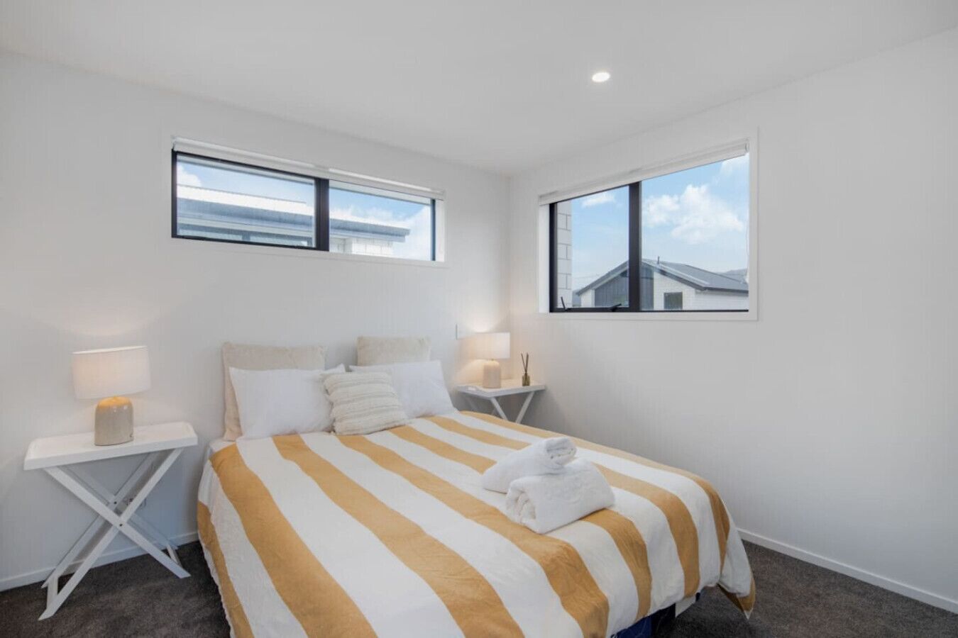 A hotel room with a large bed, two bedside tables, and two windows.