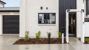 Un bâtiment moderne à deux étages, doté d’une façade en briques blanches, d’une porte de garage noire et d’une petite fenêtre.