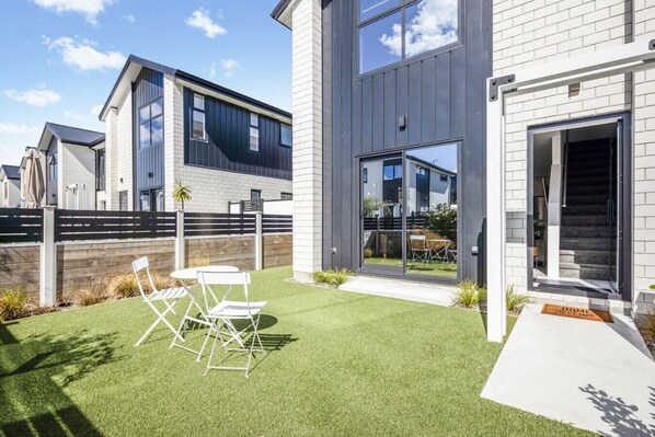 Une maison moderne dotée d’un patio, d’un coin repas avec des chaises et d’un escalier menant à l’entrée.