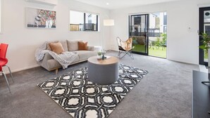 A modern living room with a grey sofa, a red chair, a patterned rug, and a coffee table. - Tranquil Trentham Escape (Upper Hutt)