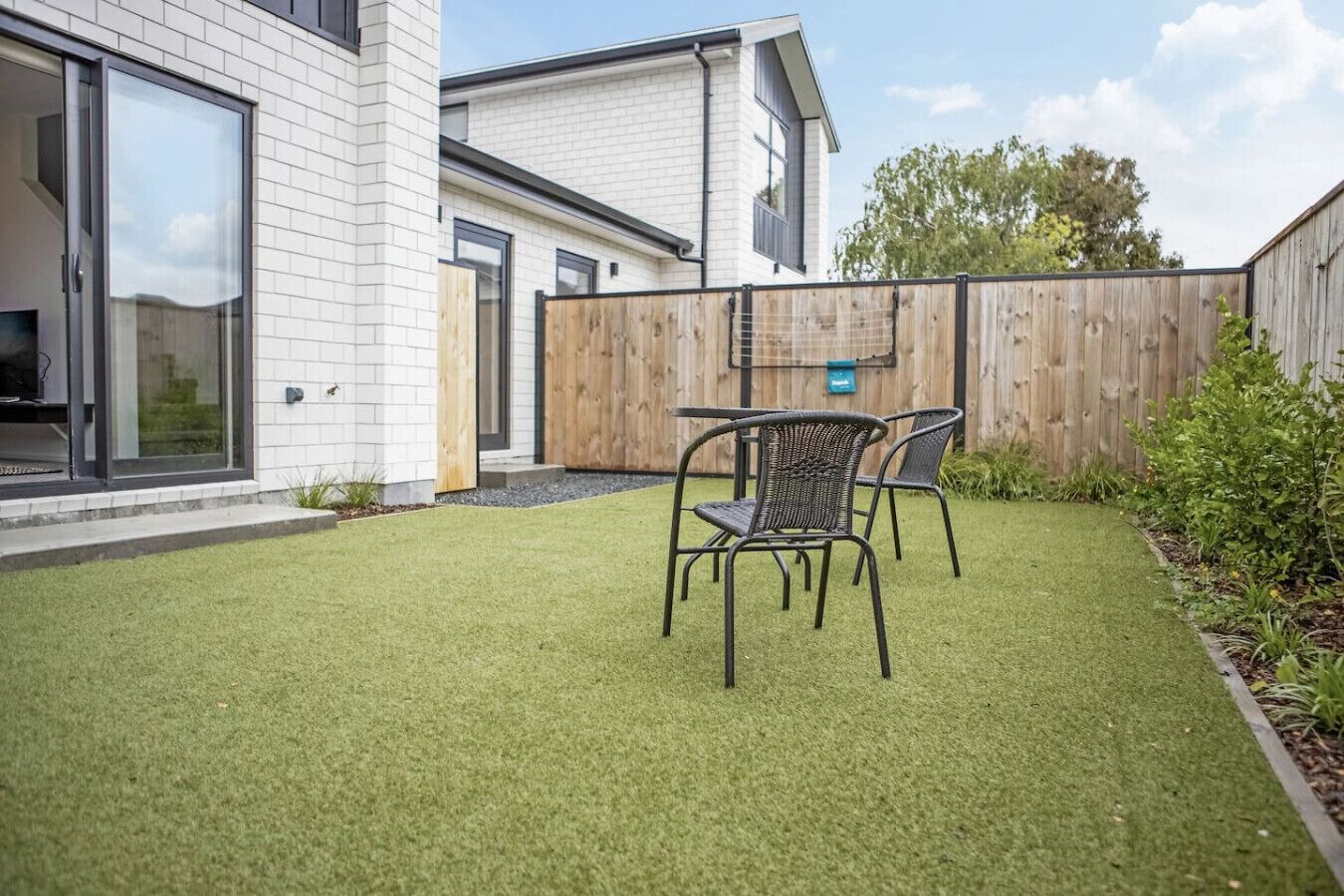 A modern house with a well-maintained lawn and a patio area with metal chairs.