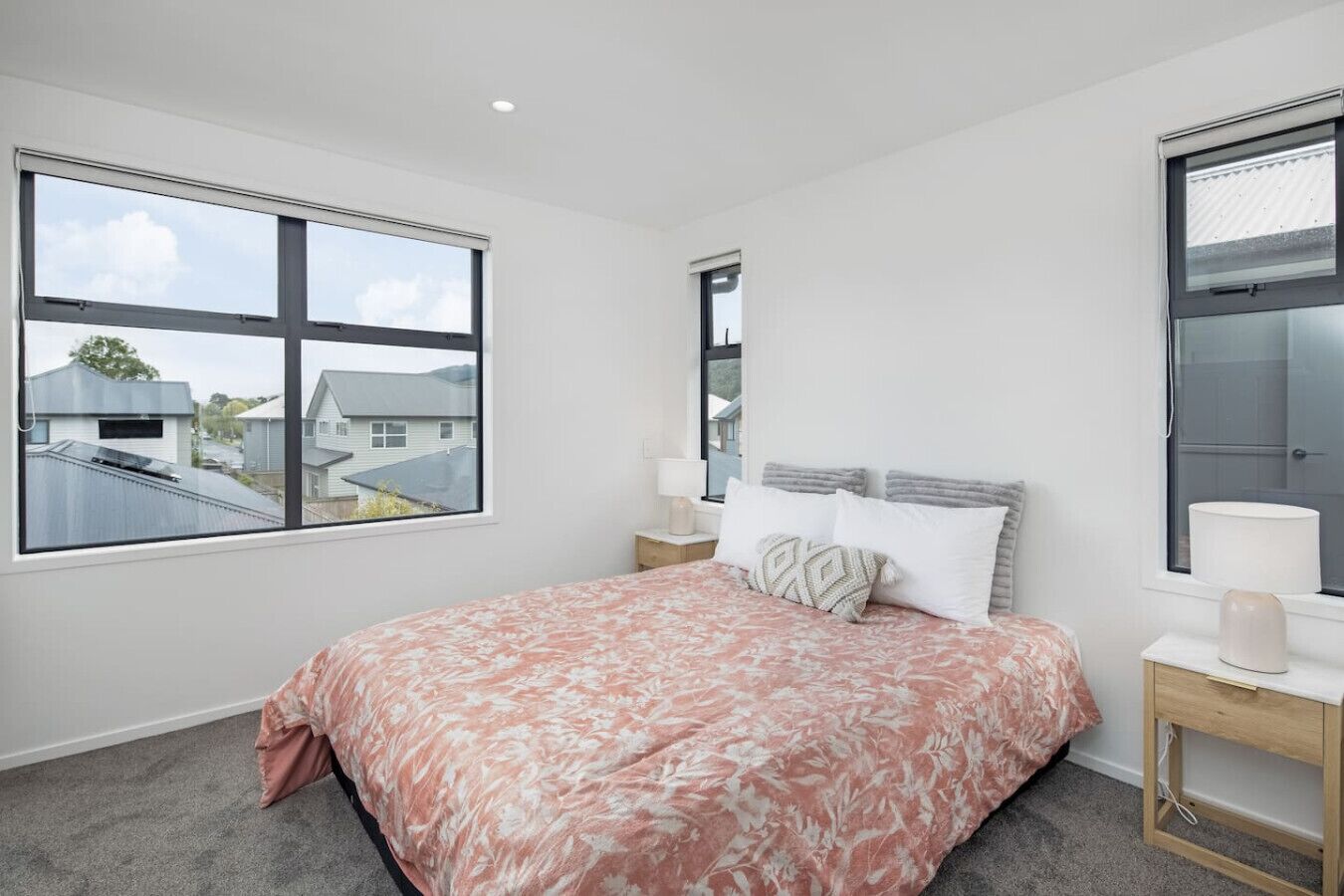 Ein Schlafzimmer mit einem großen Bett, zwei Nachttischen und einem Fenster mit Blick auf Häuser.