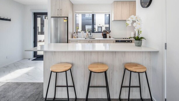 Cocina moderna con una isla grande, electrodomésticos de acero inoxidable y taburetes de madera.