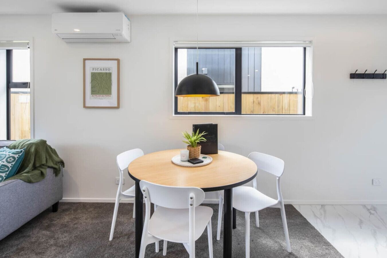 A modern dining area with a round table, white chairs, a black pendant light, and a framed map on the wall.