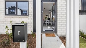 Una casa moderna con un buzón negro marcado '10', un felpudo y una puerta de cristal que da a un comedor con sillas y una mesa.