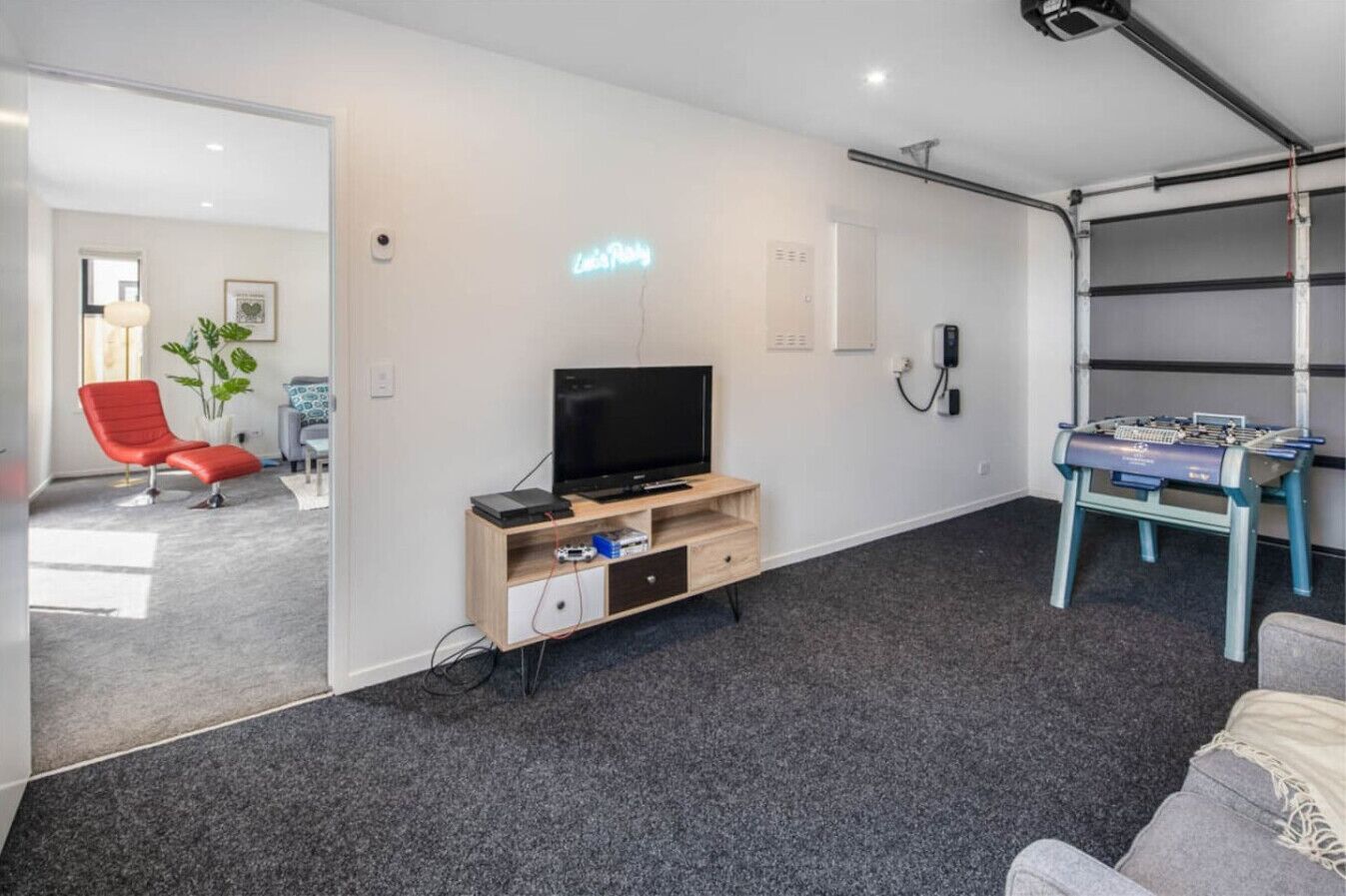 A modern living room with a flat-screen TV, a foosball table, and a red chair.
