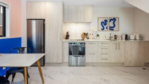 A modern kitchen with light wood cabinets, a stainless steel refrigerator, and a dishwasher. There is a dining area with a table and chairs. - Hutt Hideaway on Milne (Lower Hutt)