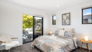 A bedroom with a large bed, a cat chair, a sliding glass door, and artwork on the walls. - Hutt Hideaway on Milne (Lower Hutt)