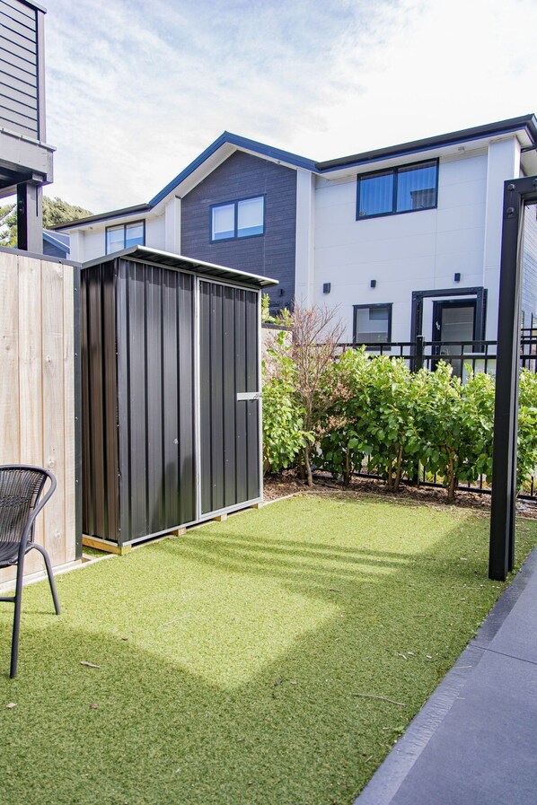 A residential backyard with artificial grass, a shed, and a patio chair. - Groveview Oasis: 1BR Retreat (Lower Hutt)