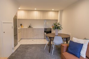 A compact kitchen with a dining area, a sofa, and a small rug. - Groveview Oasis: 1BR Retreat (Lower Hutt)