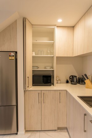 A modern kitchen with wooden cabinets, a built-in coffee machine, and a stainless steel refrigerator.