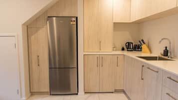 A modern kitchen with a stainless steel refrigerator, wooden cabinets, a countertop sink, and various kitchen utensils.