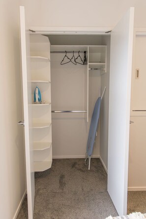 A walk-in closet with shelves, a hanging rod, and a folded item on the floor. - Groveview Oasis: 1BR Retreat (Lower Hutt)