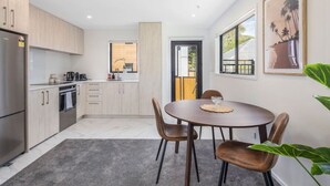 A modern kitchen with a dining area, featuring a round table with chairs, a refrigerator, and a window with a view of the outside. - Bright and Comfortable 2BR Stay on Rainey Grove (Lower Hutt)