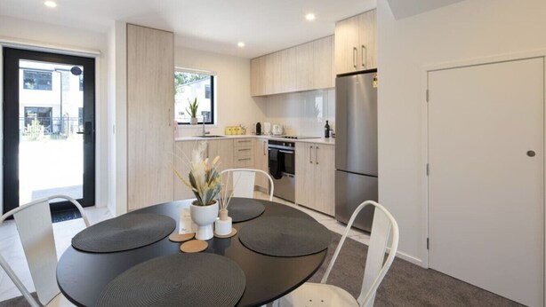 Une cuisine moderne avec des meubles en bois clair, des appareils en acier inoxydable et un coin repas comprenant une table ronde et des chaises.