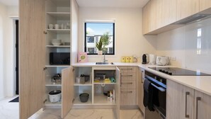 Une cuisine moderne avec des meubles en bois, un four encastré et une fenêtre donnant sur un quartier résidentiel.