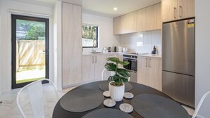 A modern kitchen with light wood cabinets, a stainless steel refrigerator, and a dining area with a round table and chairs. - Ariki Shire: A Wellington Fantasy (Lower Hutt)