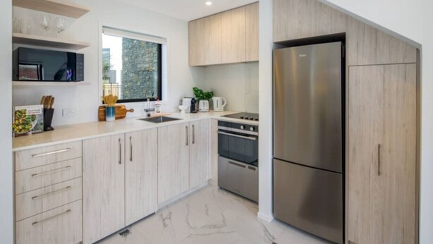 A modern kitchen with light wood cabinets, stainless steel appliances, and a large window providing natural light. - Staycation Treasure at Johnston (Lower Hutt)