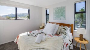 A bedroom with a bed, two bedside tables, a window with a view, and a wall-mounted artwork. - Staycation Treasure at Johnston (Lower Hutt)