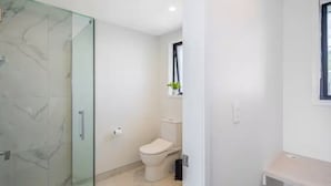A modern bathroom with a glass shower enclosure, a toilet, and a small window. - Staycation Treasure at Johnston (Lower Hutt)