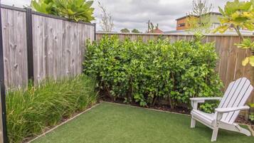 A backyard with a wooden fence, green hedges, and a white Adirondack chair.