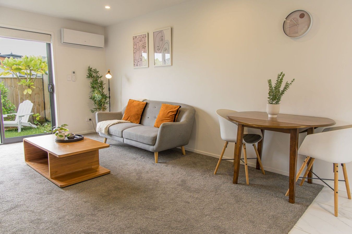 Una sala de estar moderna con un sofá gris, una mesa de centro de madera, una mesa de comedor con sillas y un ventanal grande.